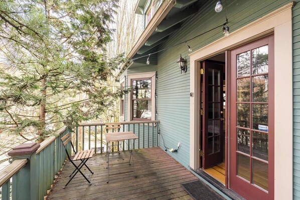 A wooden deck with a bench and a table, a door with a window, and a string of lights.