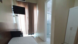 Ένα δωμάτιο ξενοδοχείου με ένα κρεβάτι, ένα γραφείο, μια ντουλάπα και ένα μπάνιο, το οποίο φαίνεται μέσα από μια γυάλινη πόρτα.