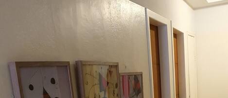 Un pasillo con tres cuadros abstractos en la pared y una puerta al final.