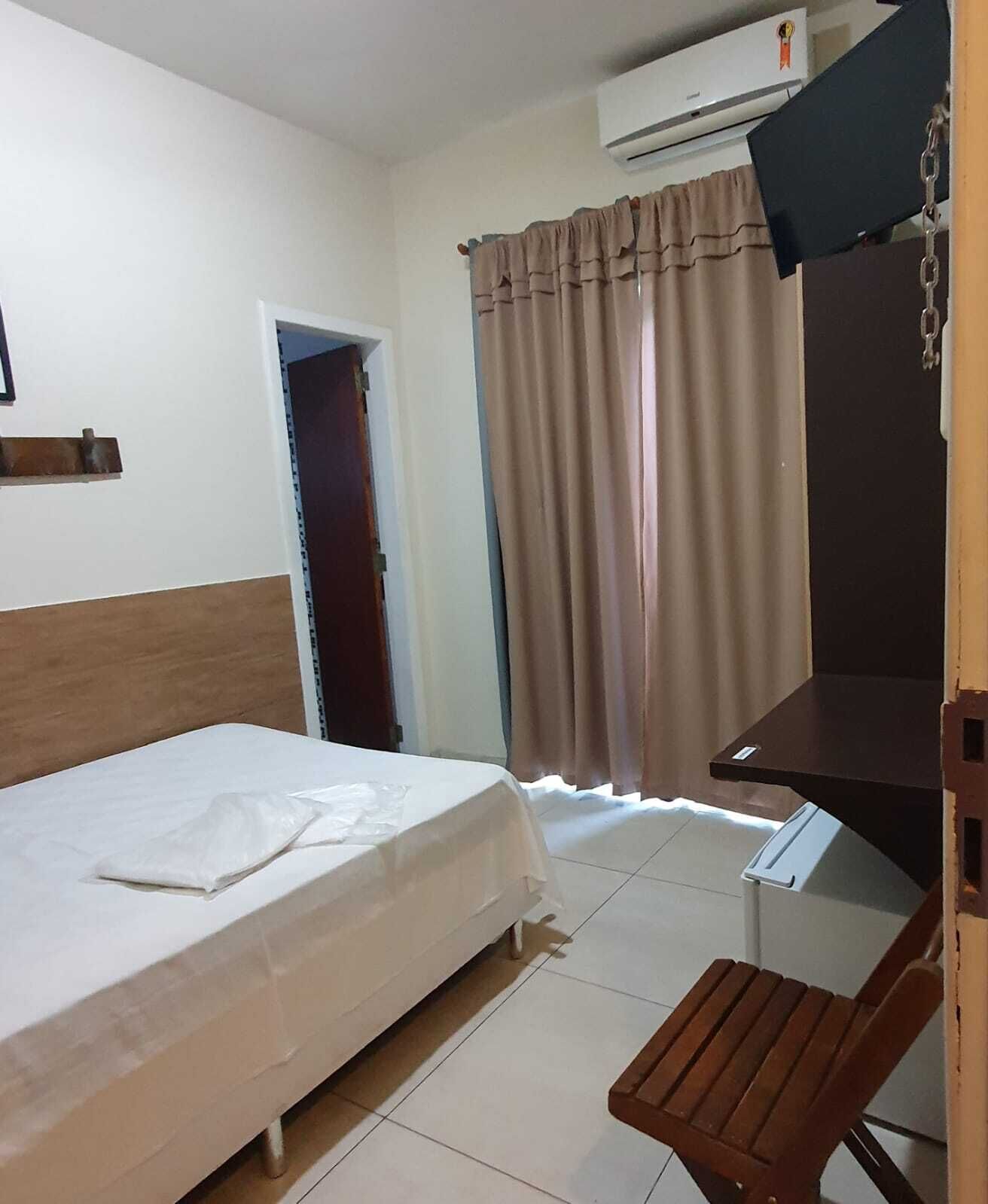 Una habitación de hotel con cama, escritorio, silla, televisor y ventana con cortinas.