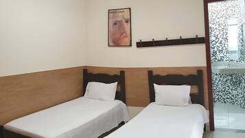 A room with two single beds, a wooden headboard, a white wall, and a poster of the Van Gogh Museum.