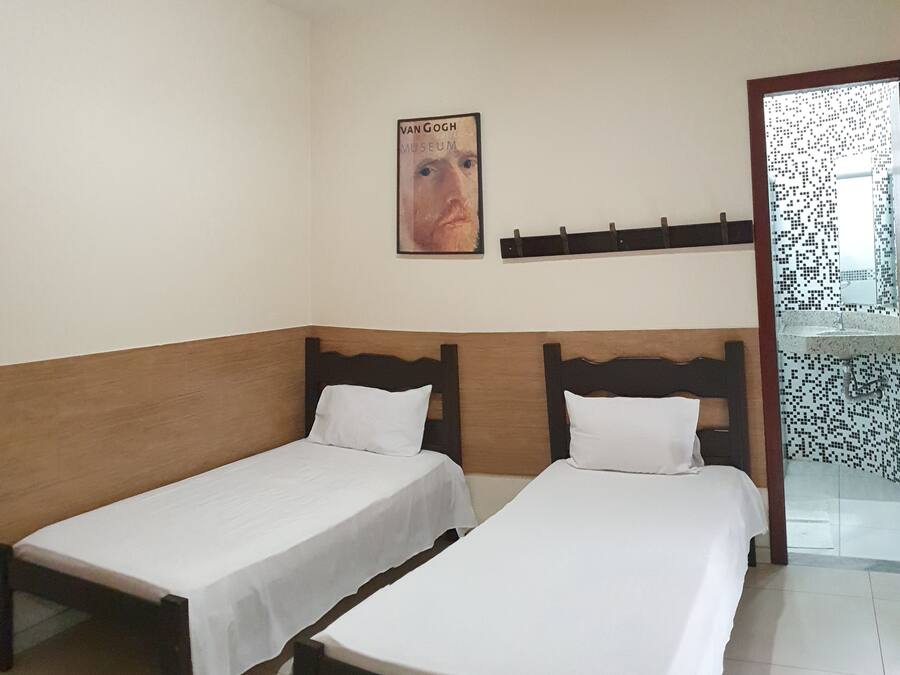 A room with two single beds, a wooden headboard, a white wall, and a poster of the Van Gogh Museum.
