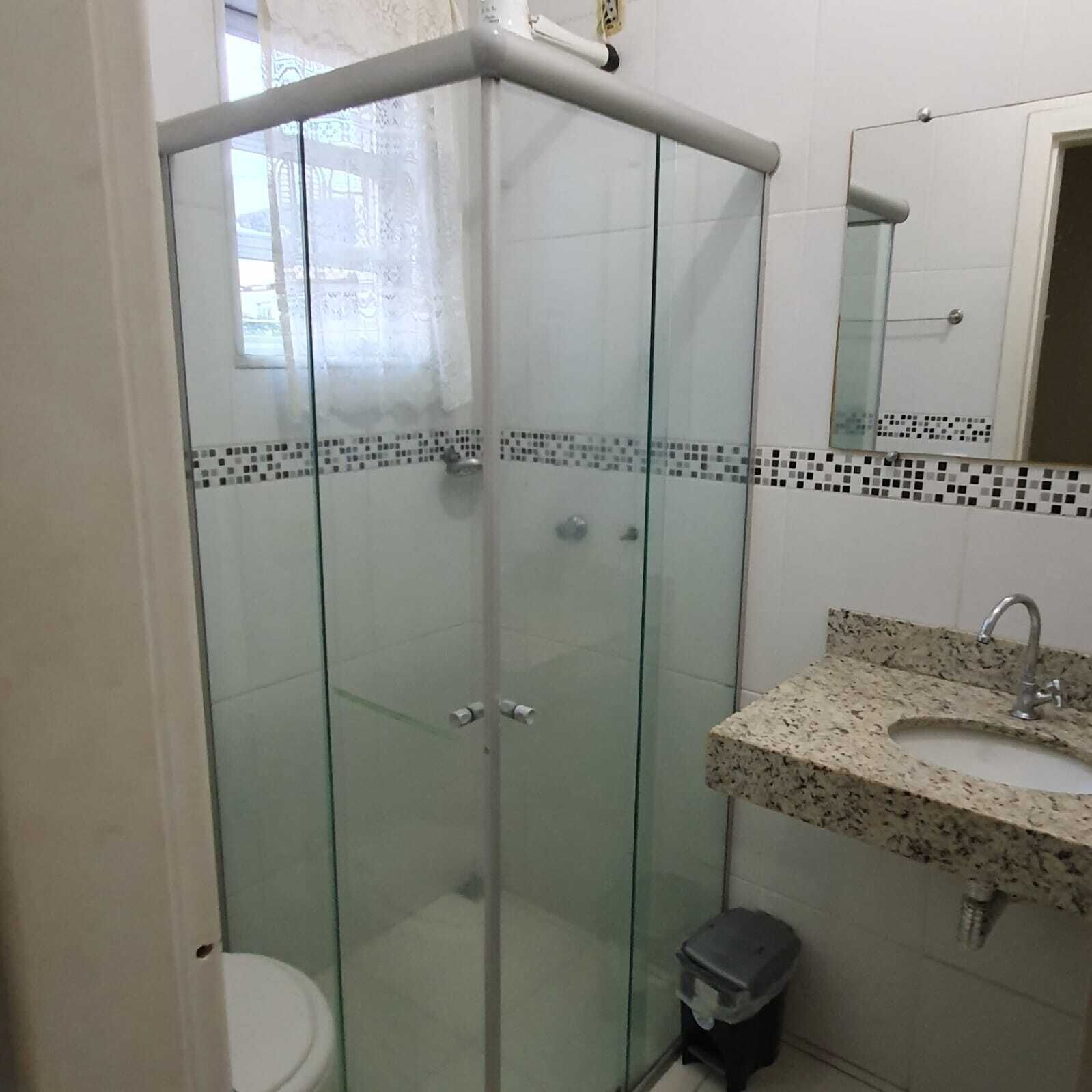 A glass-enclosed shower with a tiled floor, a sink with a granite countertop, and a mirror above the sink.