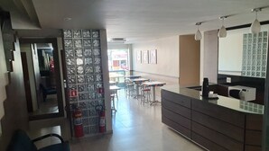 Ένας σύγχρονος χώρος υποδοχής ξενοδοχείου με γραφείο υποδοχής, χώρο αναμονής και ένα γυάλινο διαχωριστικό με πυροσβεστήρες.