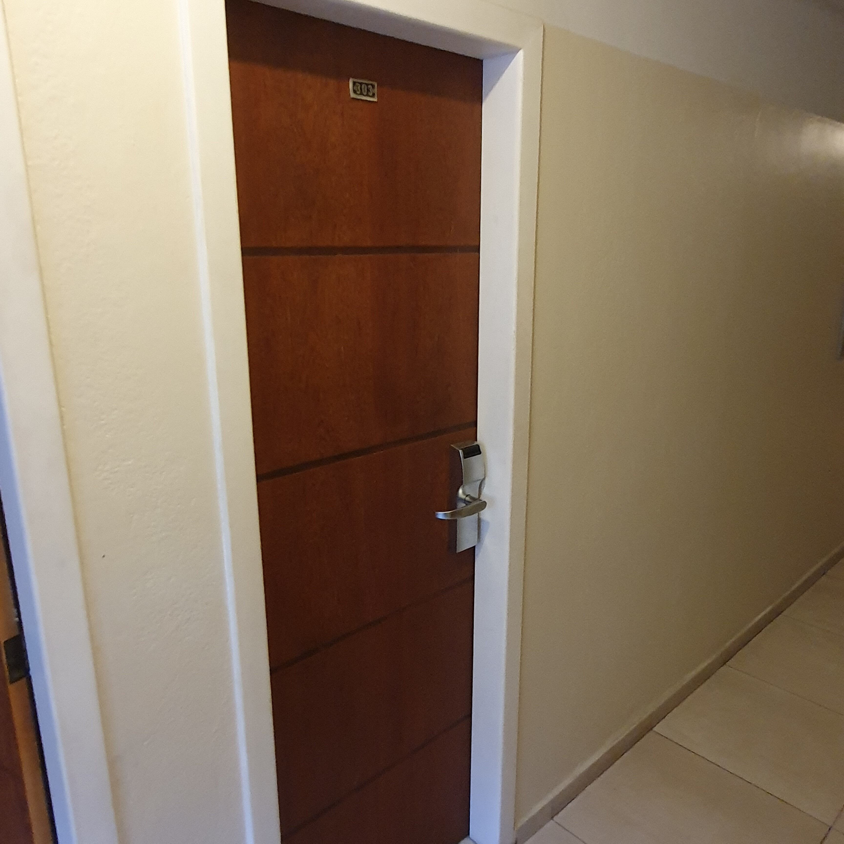 Un corridoio con una porta in legno, pareti bianche e pavimento piastrellato.