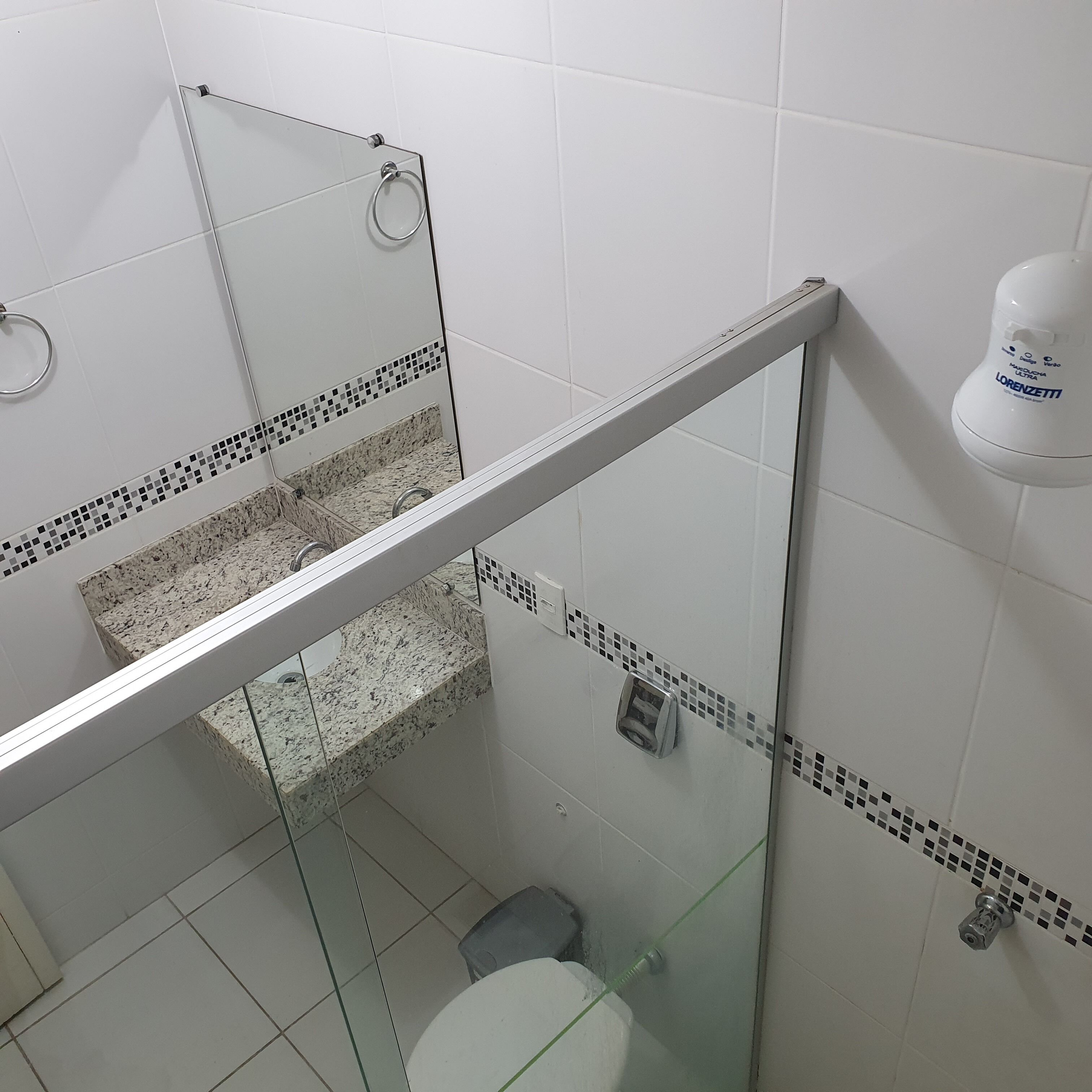 A modern bathroom with a glass shower enclosure, a toilet, and a hand dryer.