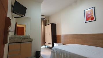 Habitación de hotel con cama, televisión montada en la pared, armario y un cartel en la pared.