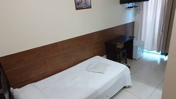 A hotel room with a single bed, a desk, a chair, a TV mounted on the wall, and a window with curtains.