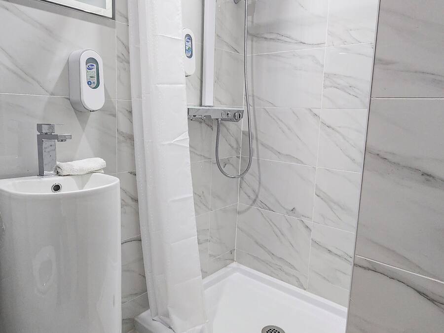 Une salle de bain moderne avec un sol en marbre, un lavabo doté d’un distributeur de savon, une douche avec un pommeau de douche à main et une cabine de douche en verre.