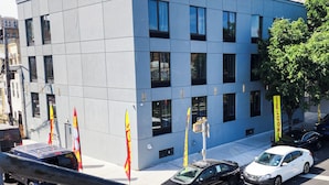 A modern building with a flat facade, multiple windows, and a parking area with cars and flags. - HOTEL FUEGO BRONX (Bronx)