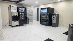 A clean, modern lobby with two vending machines, one dispensing snacks and the other cold drinks, and a trash bin. - HOTEL FUEGO BRONX (Bronx)