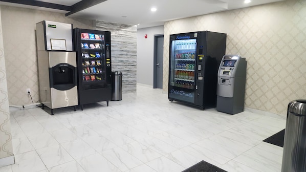 Eine saubere, moderne Lobby mit zwei Automaten: einem für Snacks und einem für kalte Getränke, sowie einem Mülleimer.