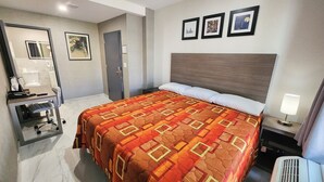 A hotel room with a bed, a desk with a chair, a mirror, and a door. There are three framed pictures on the wall. - HOTEL FUEGO BRONX (Bronx)