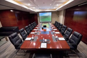 Une salle de conférence avec une longue table, des chaises noires et un écran de projection.
