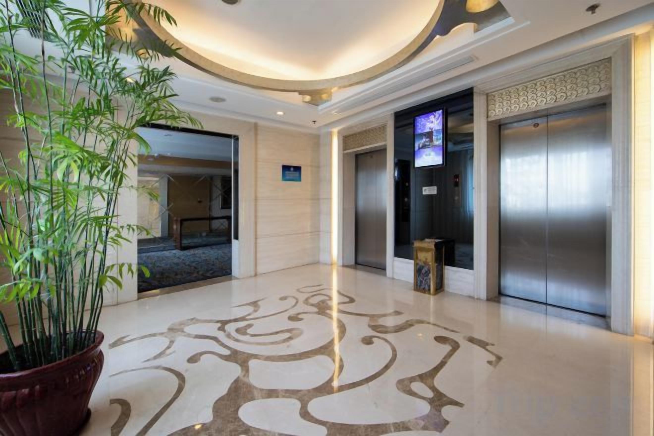 A lobby with a large potted plant, a modern elevator, and a television screen.