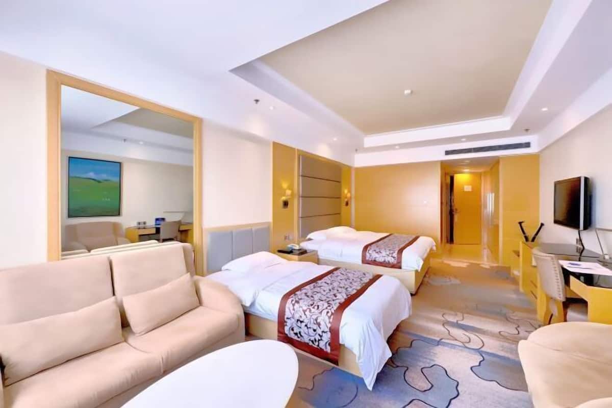 Habitación de hotel con dos camas, un sofá, un escritorio, un televisor y un espejo grande.