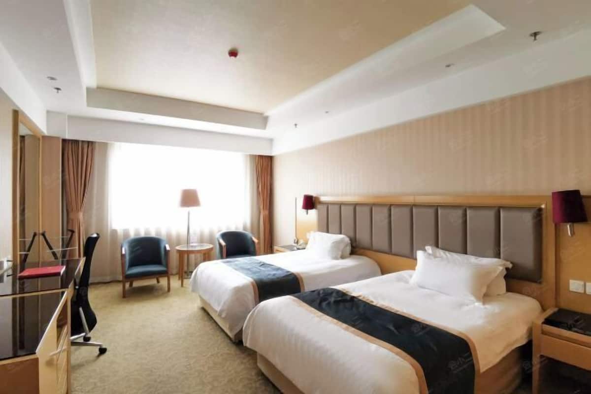 Habitación de hotel con dos camas, un escritorio, una silla y una lámpara.