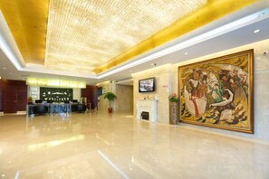 Un hall d’hôtel comprenant un comptoir d’accueil, une grande fresque murale et un lustre.