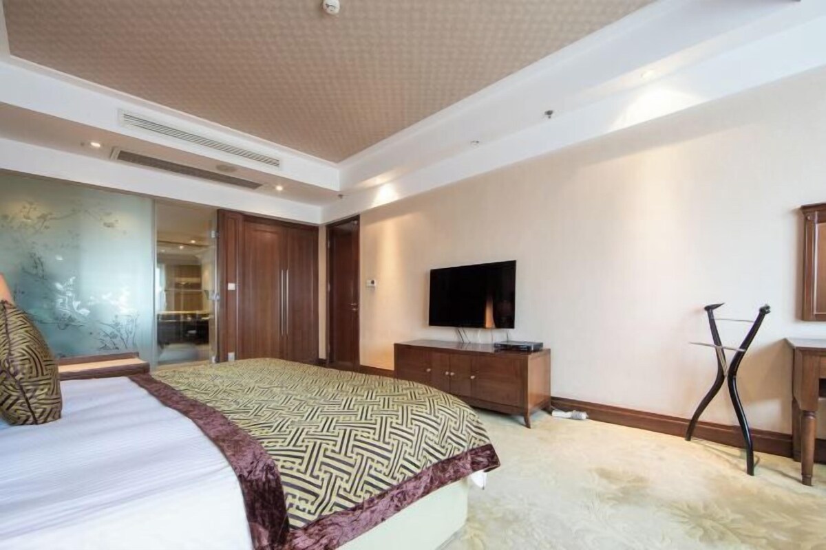 A bedroom with a bed, a TV, a wooden dresser, and a mirror.