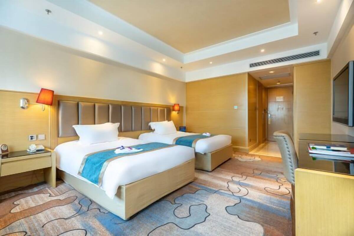 Habitación de hotel con dos camas, un escritorio y un televisor.