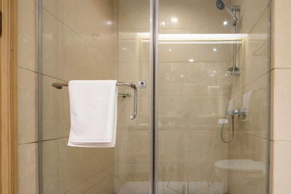 A glass-enclosed shower with a white towel on a rack, a handheld showerhead, and a wall-mounted faucet.