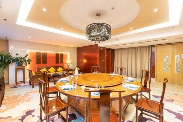 A round dining table with chairs, a chandelier, and a carpeted floor.