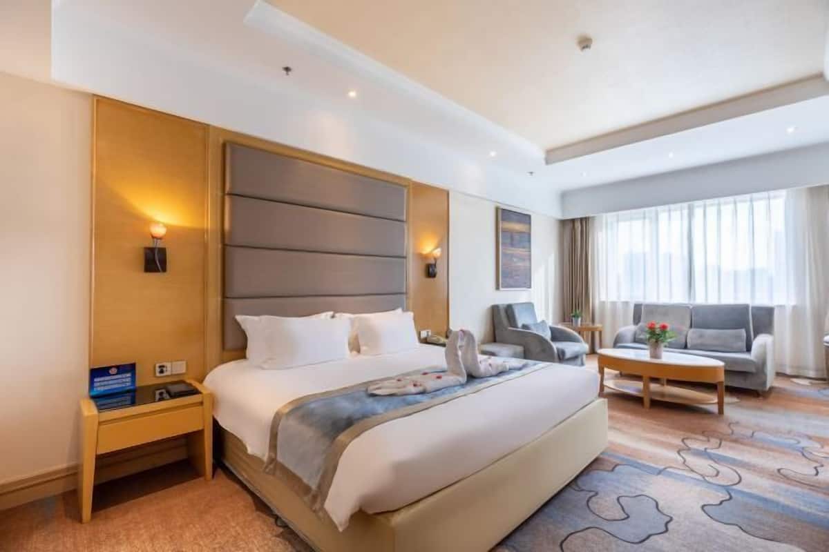 Habitación de hotel con una cama grande, una mesita de noche, un sofá, una mesa de centro y vistas al exterior.