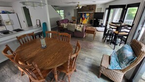 Amplia sala de estar con una mesa de comedor de madera, asientos cómodos, una chimenea de piedra y ventanas grandes que ofrecen luz natural.