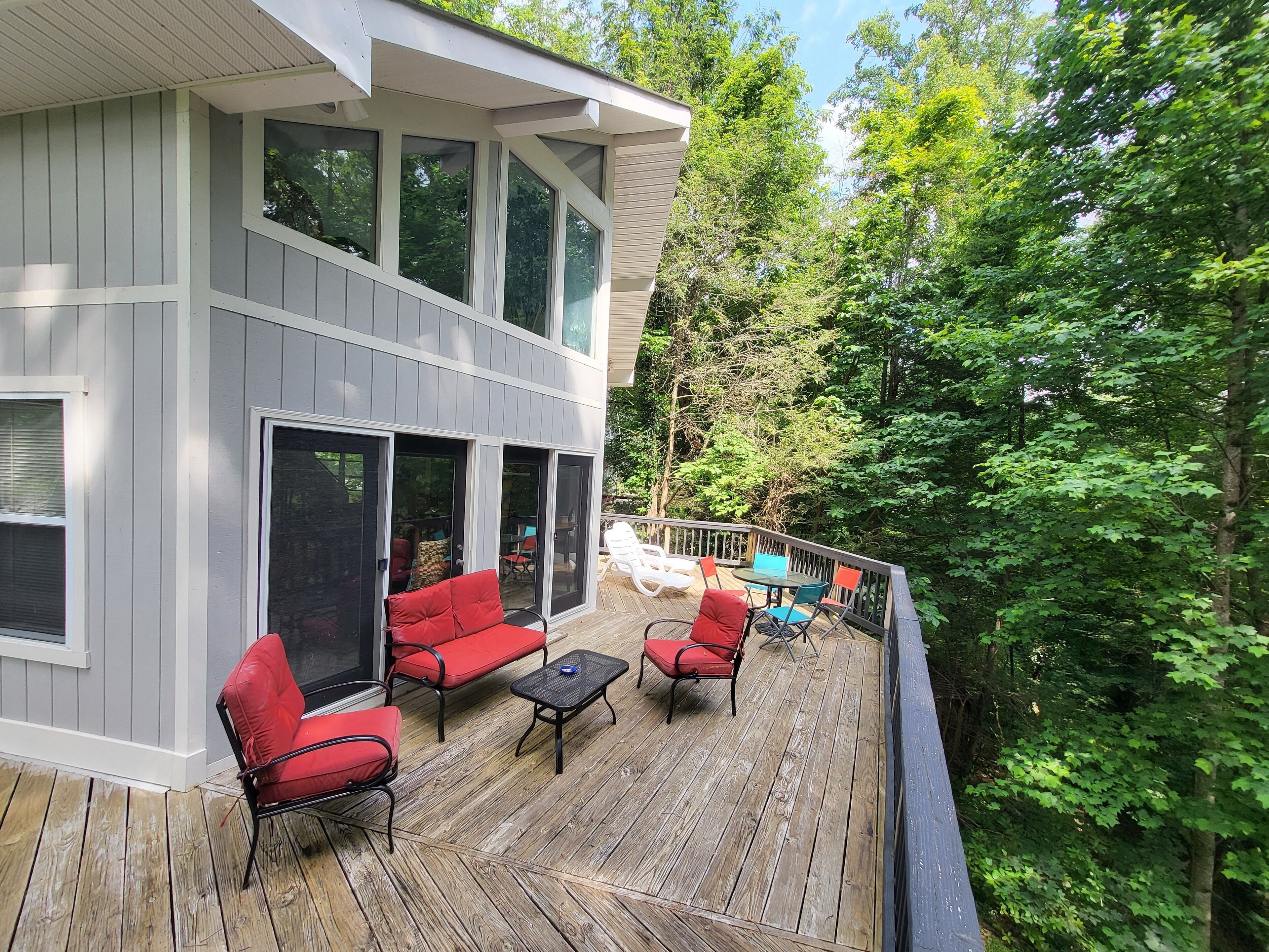 A two-story house with a deck featuring outdoor furniture and a view of the surrounding forest.