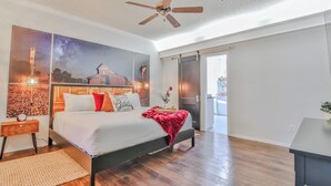 Ruime slaapkamer met een groot bed, een plafondventilator en een muurschildering van een nachthemel.