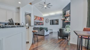 Een ruime woonkamer met een keuken, een eettafel en een grijze bank.