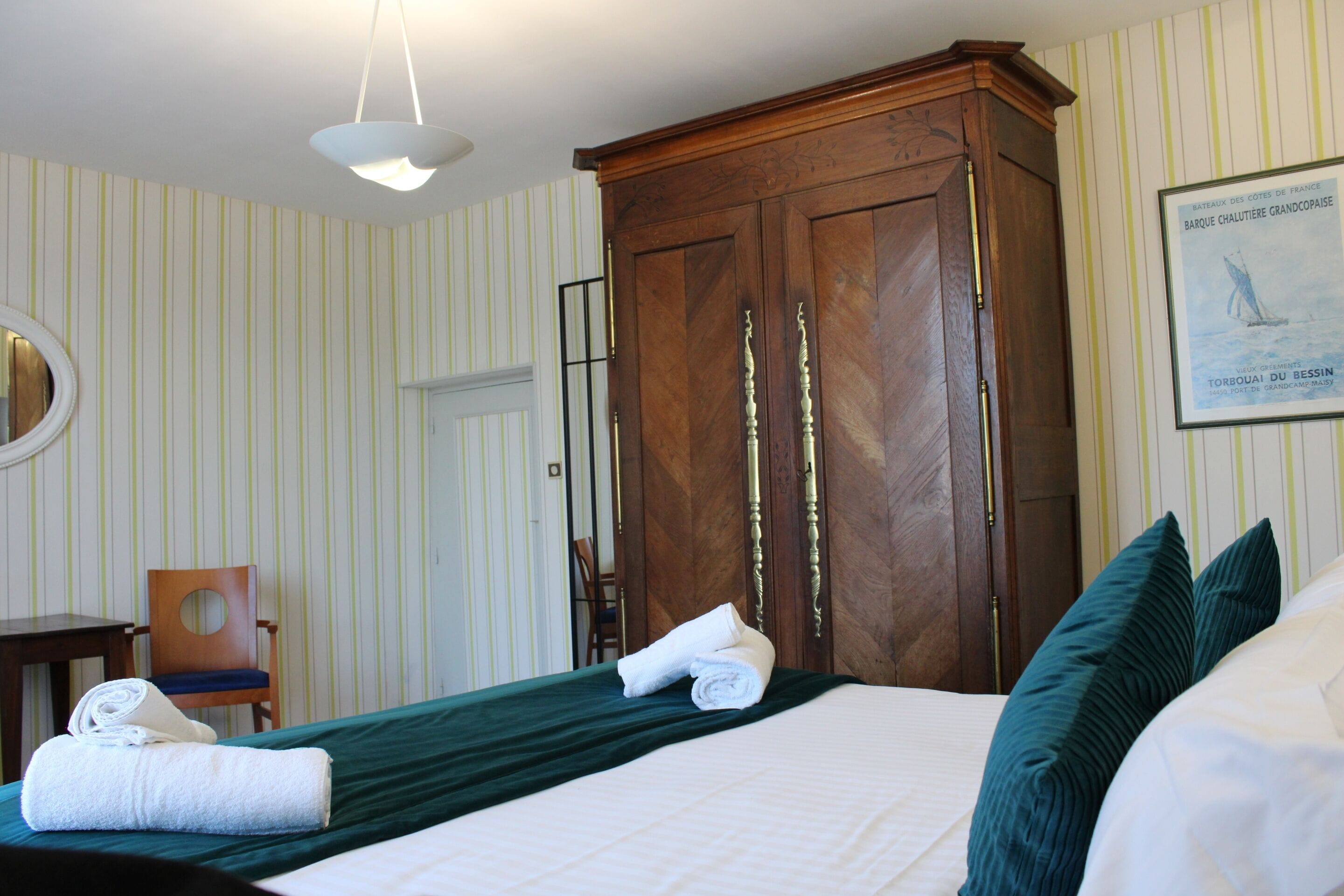 A hotel room with a large bed, a wooden wardrobe, a chair, and a framed picture on the wall.