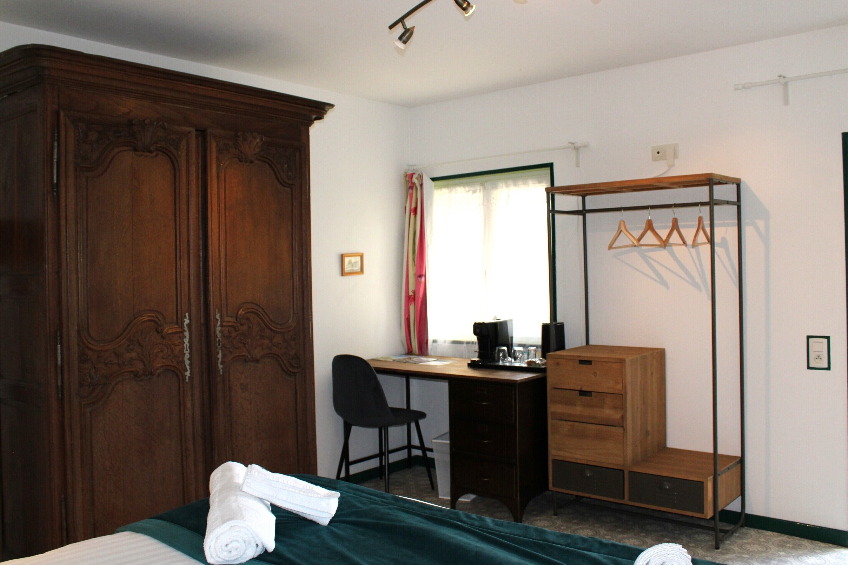 Un dormitorio con cama, escritorio, silla, armario y perchero.
