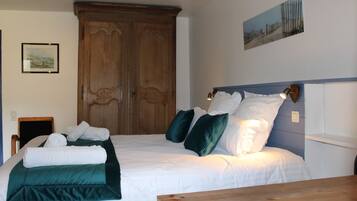 Een netjes opgemaakt bed met witte lakens en groene accenten, een houten garderobe en een lijst met een afbeelding aan de muur.