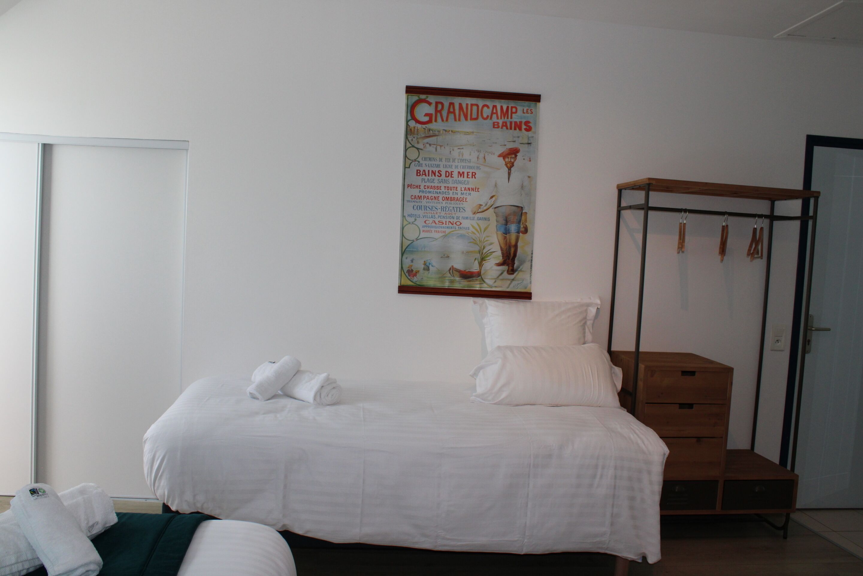 A hotel room with a bed, a wooden dresser, and a poster on the wall.