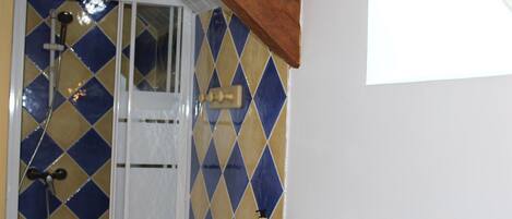 Un baño con ducha, una puerta blanca y una botella de champú sobre el mostrador.