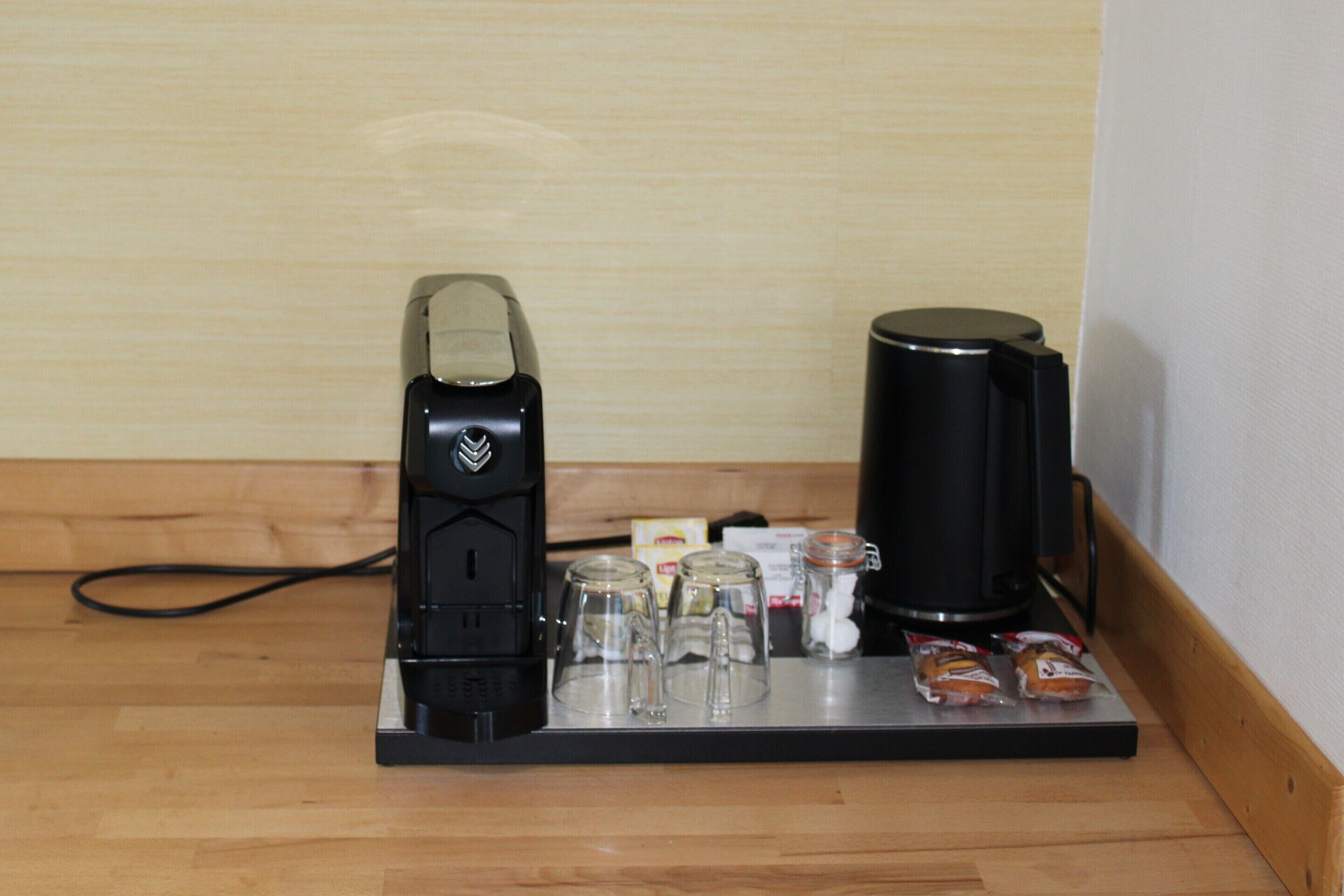 A coffee maker and a water dispenser on a wooden counter with glass cups and sugar packets.