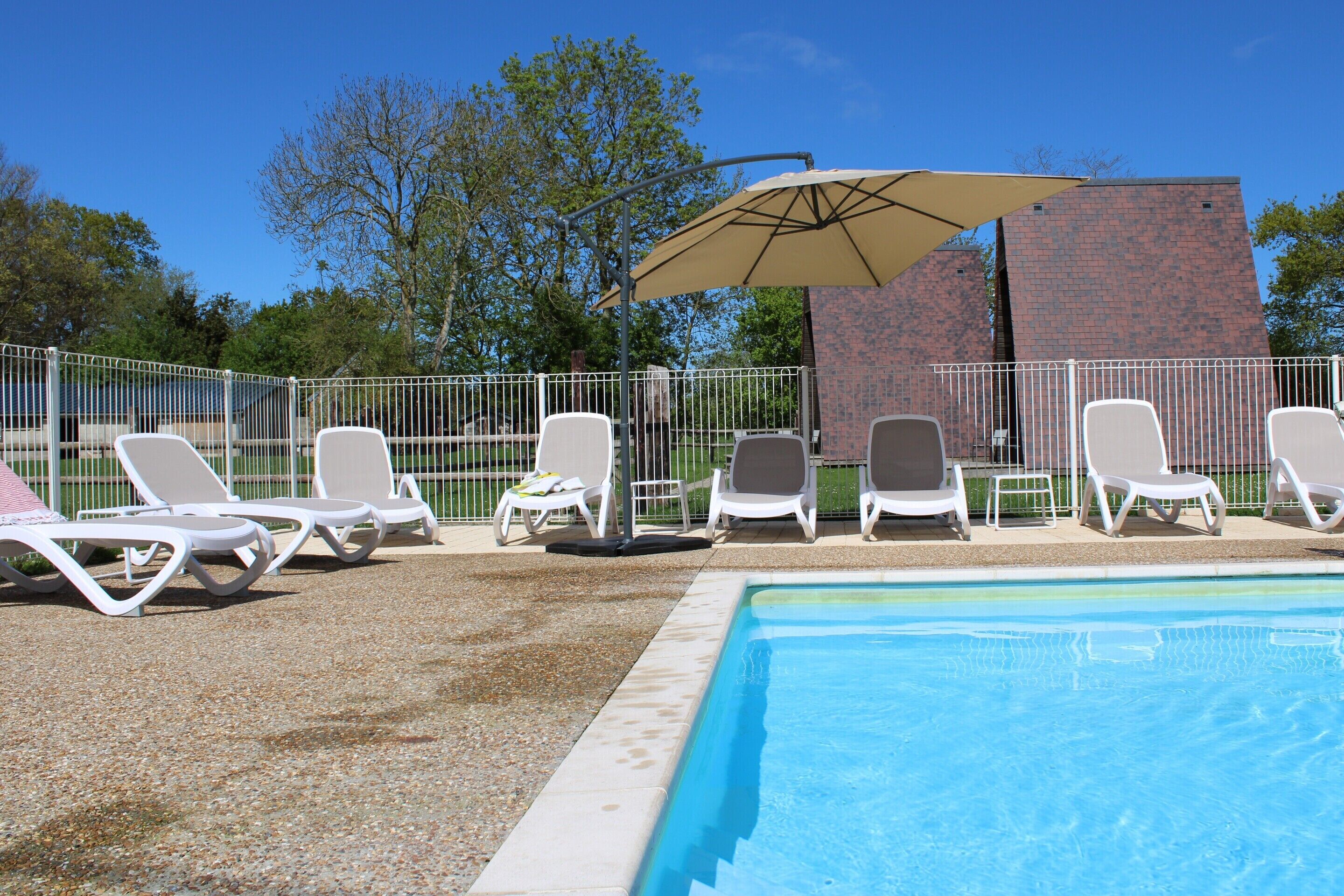 Area piscina con lettini bianchi e un ombrellone color beige.