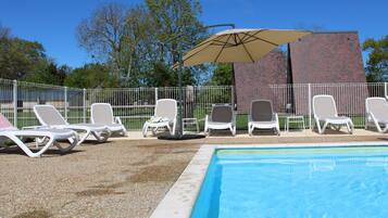 Area piscina con lettini bianchi e un ombrellone color beige.