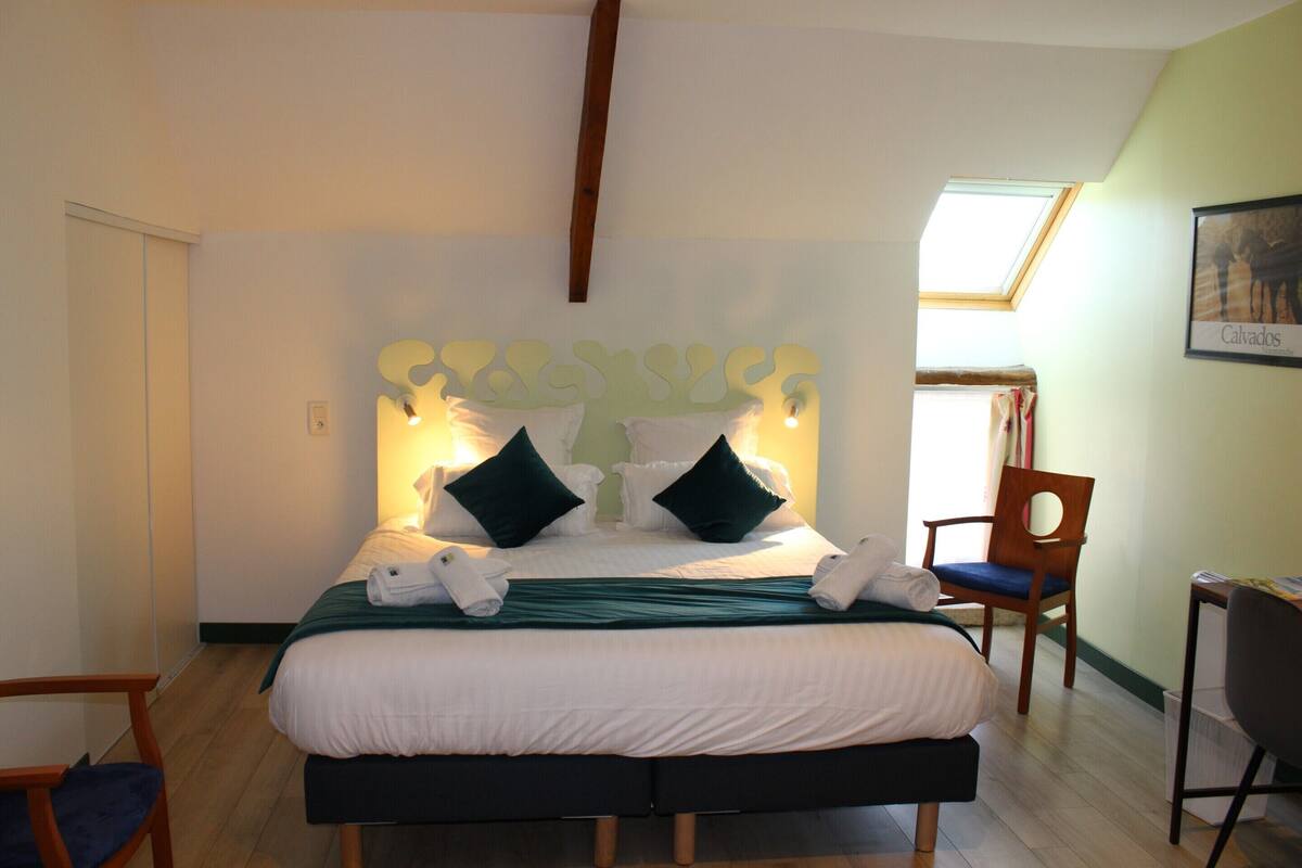 A neatly made bed with a headboard, a chair, and a desk in a room with a skylight.