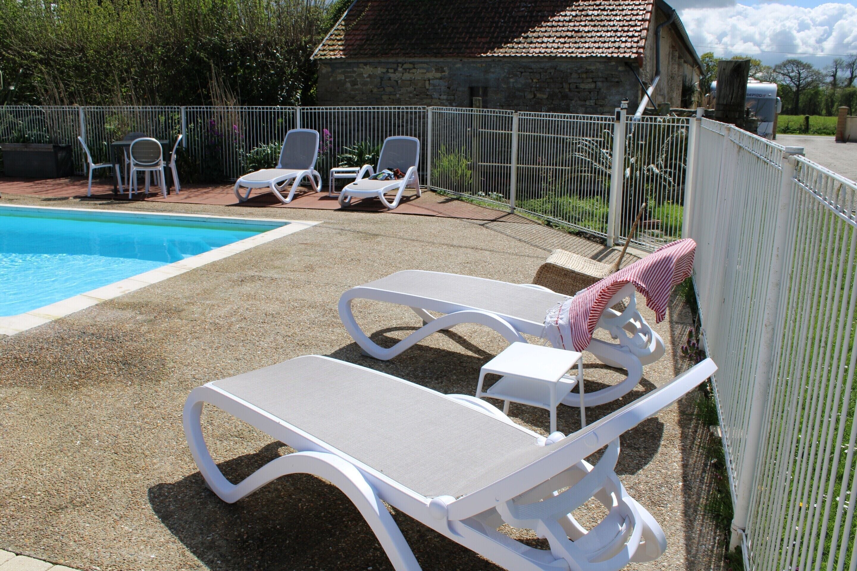 Une piscine entourée d’une clôture blanche, avec des chaises longues et une table à proximité.