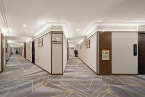 A hotel corridor with doors, framed pictures, and a carpeted floor.