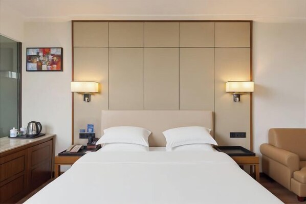 A hotel room with a large bed, two bedside lamps, a nightstand, a chair, and a desk with a lamp.