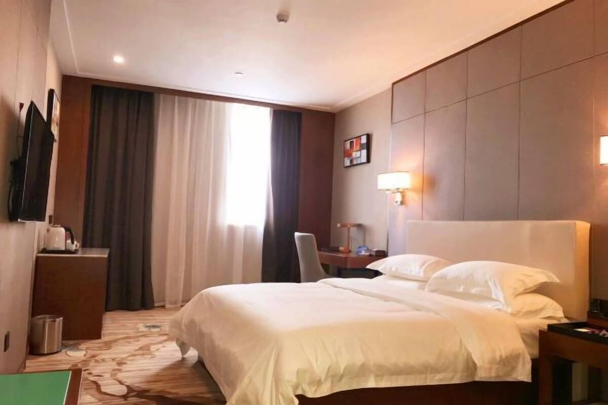 Een hotelkamer met een groot bed, een bureau met stoel, een flatscreen televisie, een lamp en een raam met gordijnen.
