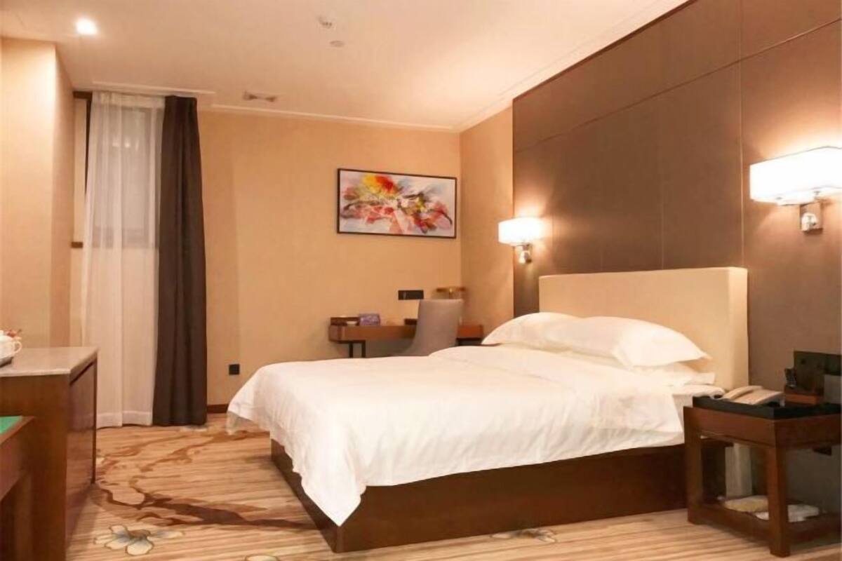 Een hotelkamer met een bed, een bureau, een stoel, een lamp en een schilderij aan de muur.