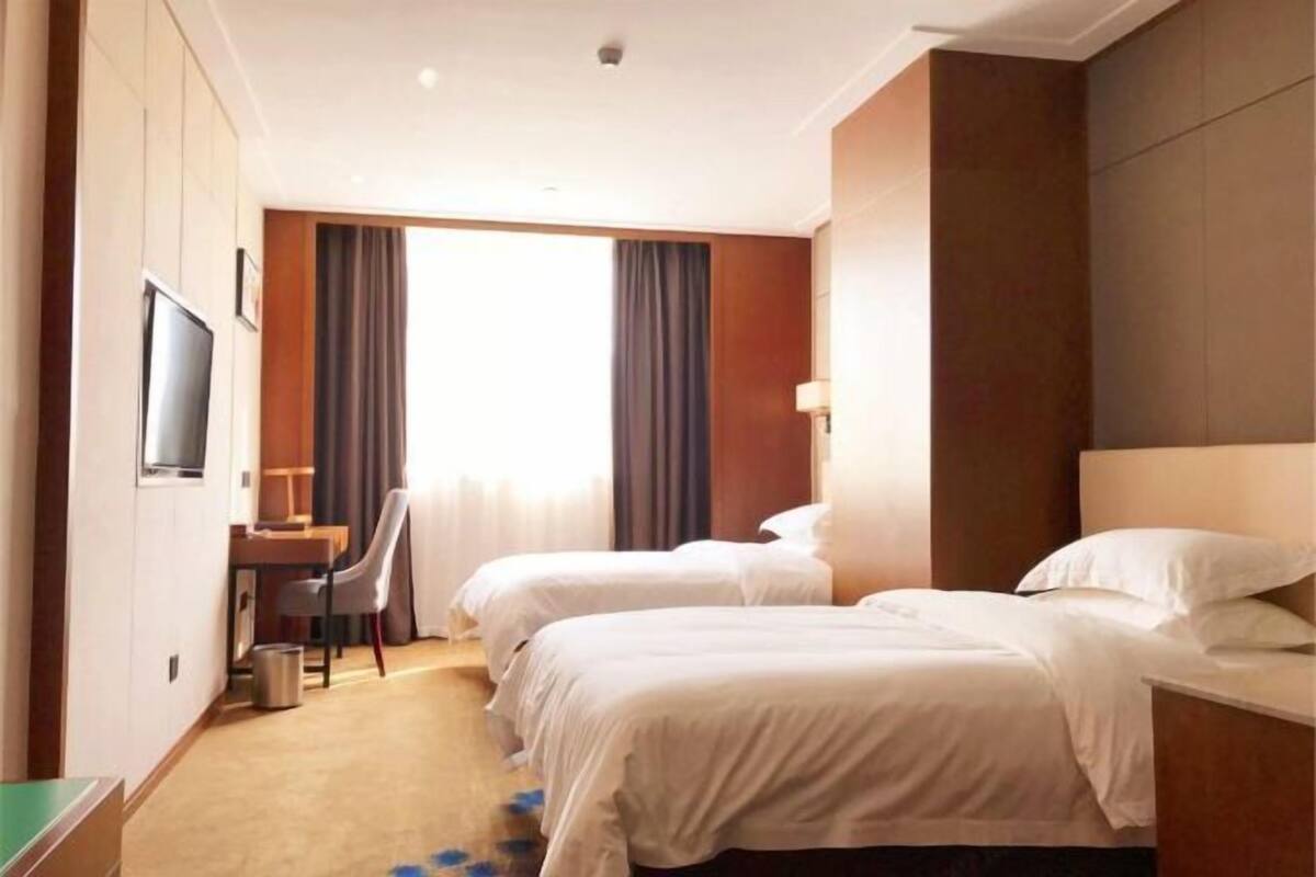 Een hotelkamer met twee bedden, een bureau, een stoel, een televisie en een groot raam met gordijnen.