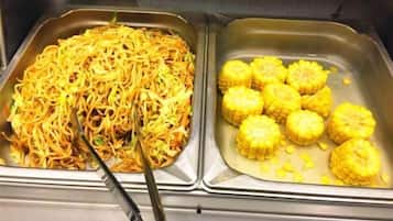 Ein Buffet mit zwei Tabletts: eines mit Nudeln und das andere mit Maiskolben.