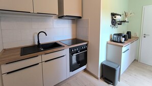 A compact kitchen with a sink, stove, oven, and a trash bin.