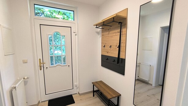 A hallway with a white door, a bench, a mirror, and a wooden shelf.