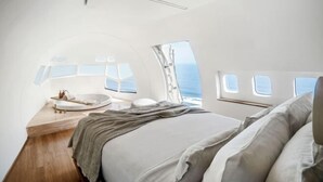 A modern, compact bedroom with a bed, a small seating area, and a view of the ocean through windows. - Private Jet Villa Uluwatu (Bali)